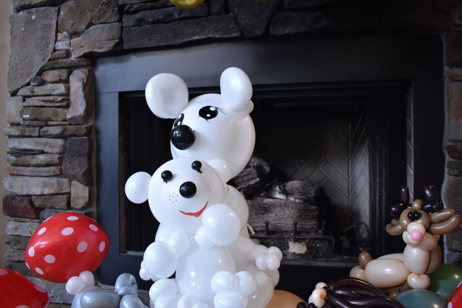 Balloon sculptures: two white bears with black eyes and nose in front of a fireplace.