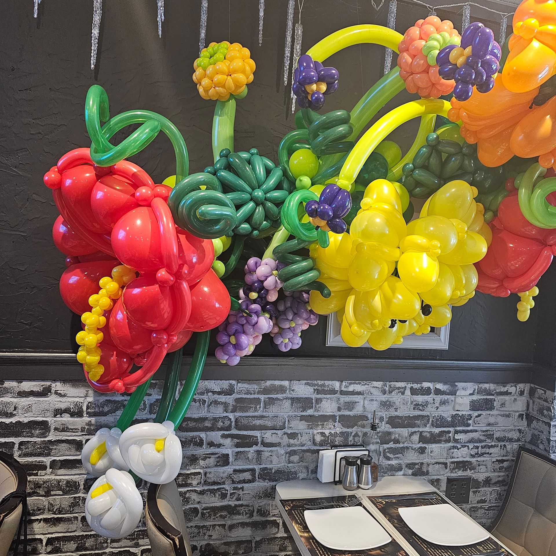 Balloon floral arrangement with red, yellow, and purple flowers, on a brick wall background.