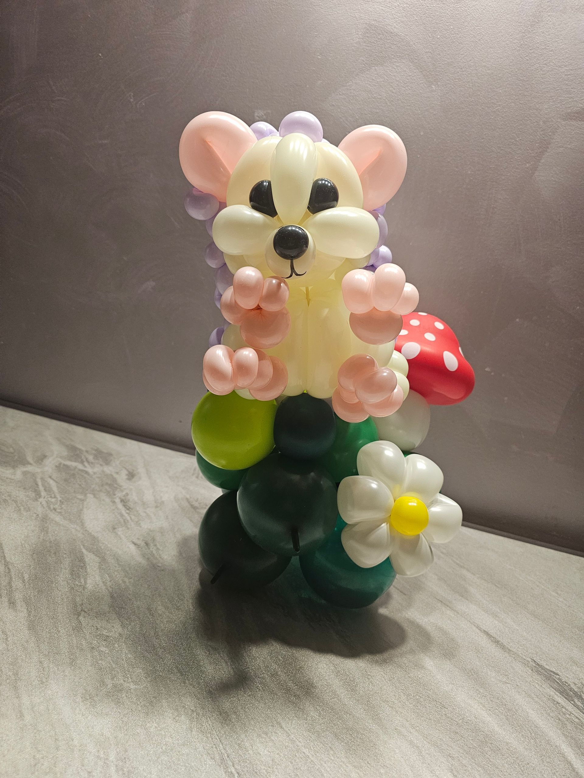 Balloon sculpture of a mouse on a green base with a flower, mushroom, and purple spiky back.