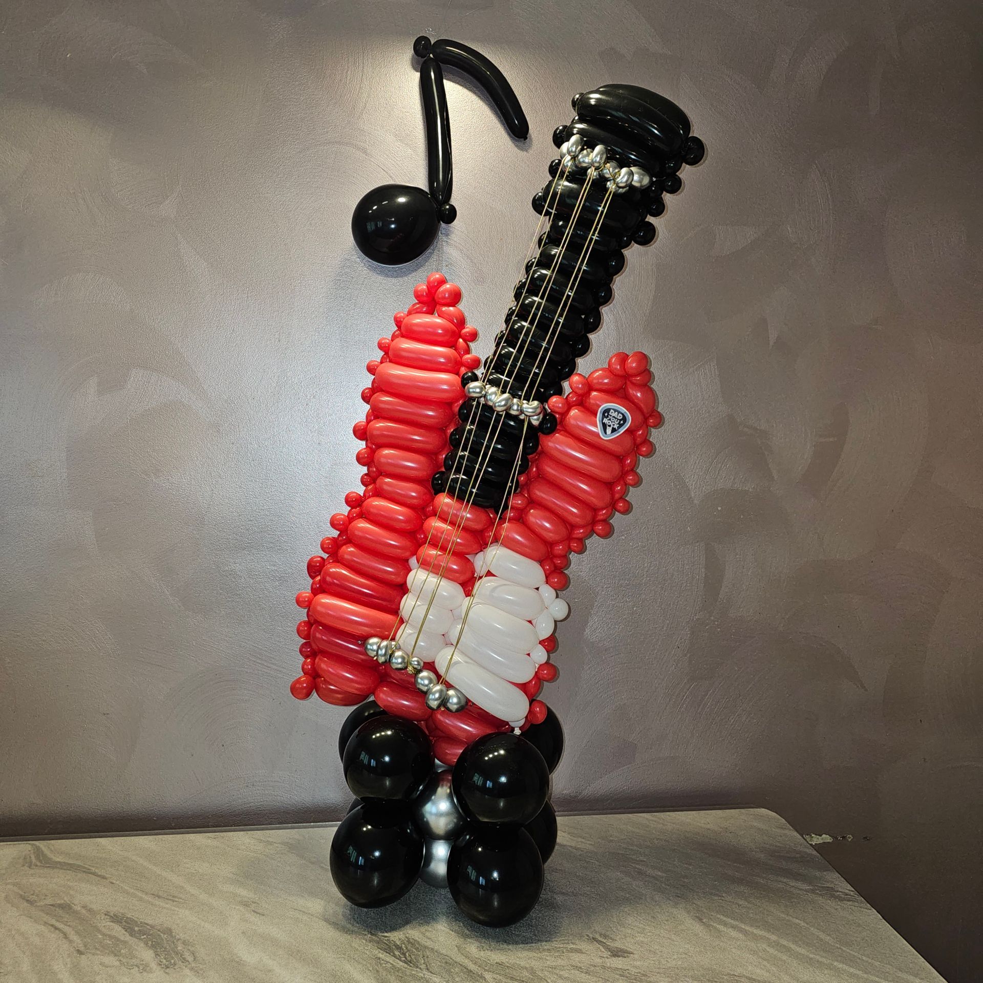 A red and black balloon guitar sculpture with a musical note, displayed on a surface.