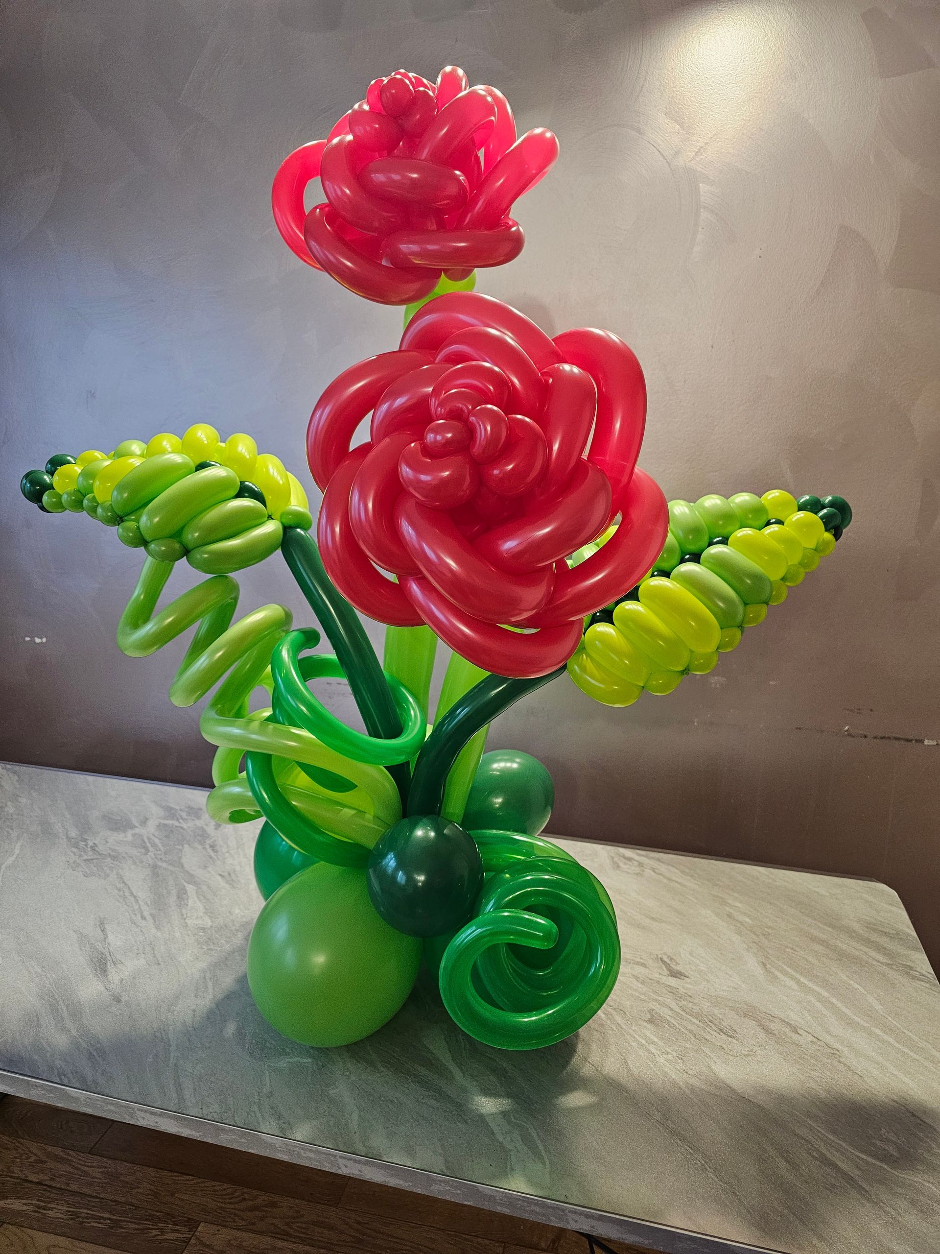 Balloon sculpture of red roses and green leaves on a table.