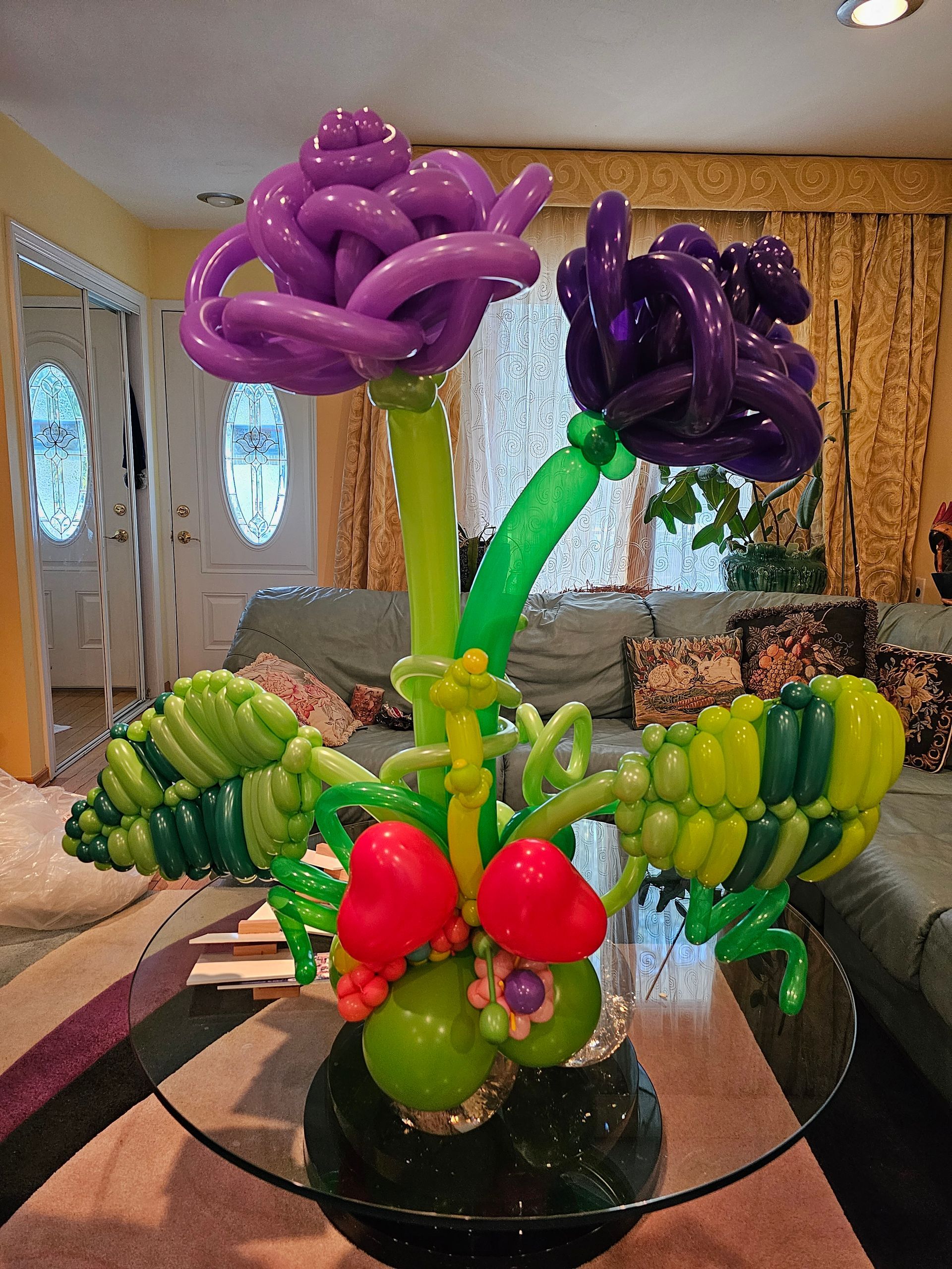 Balloon sculpture of purple and green flowers, berries, and leaves on a glass table.
