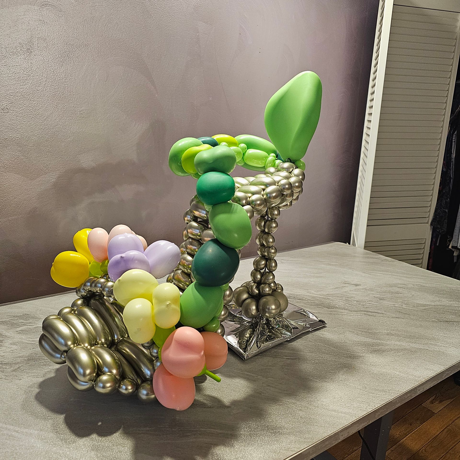 A whimsical high-heeled shoe sculpture made of shiny metallic and colorful balloons, on a table.