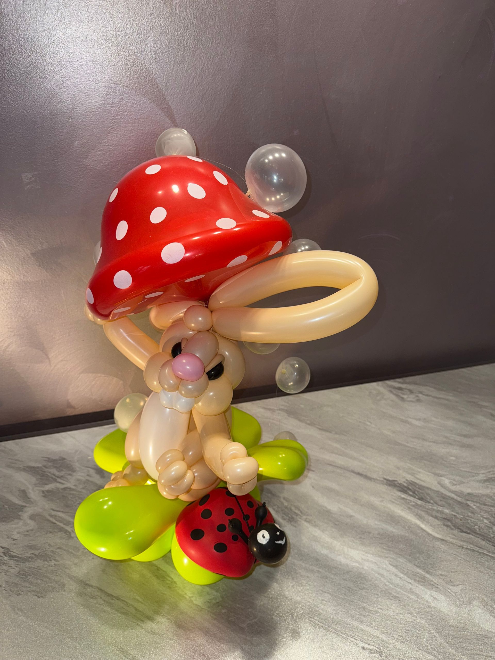 Balloon sculpture of a bunny holding a red mushroom cap, with a ladybug.