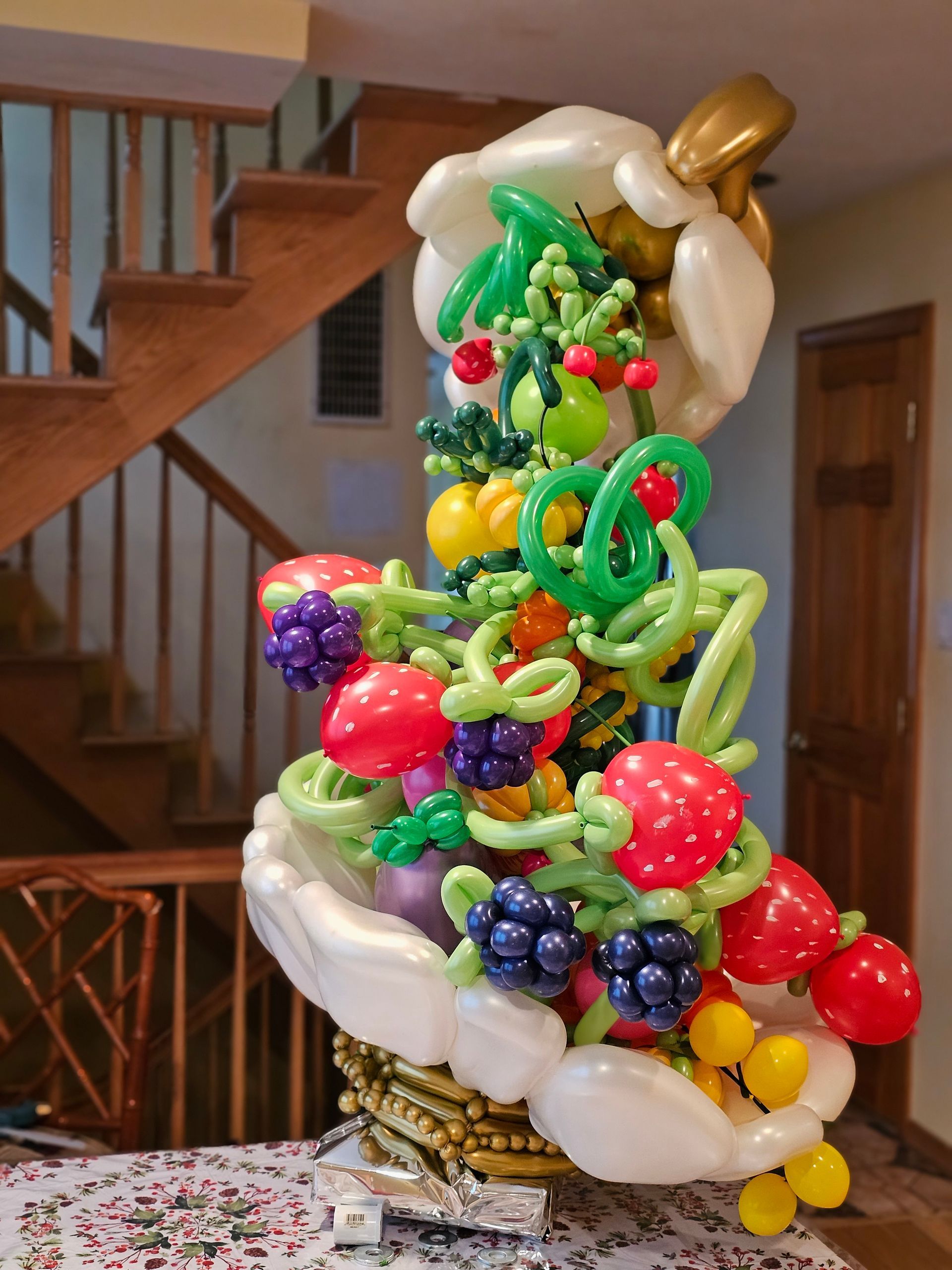 Balloon sculpture of a fruit basket with assorted colorful balloons, indoors near stairs.