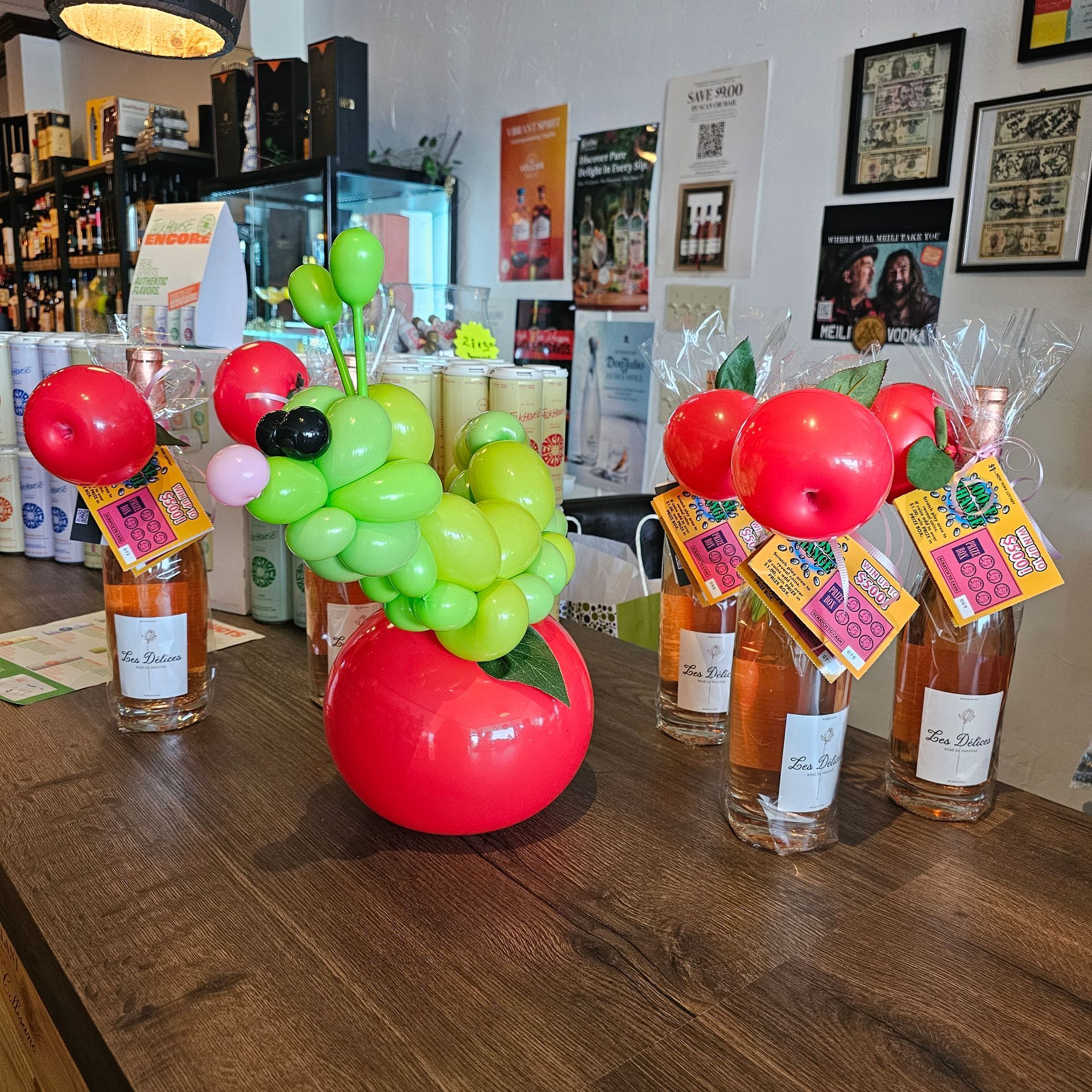 Wine bottles with apple decorations, display at a store with balloon art, showcasing products.