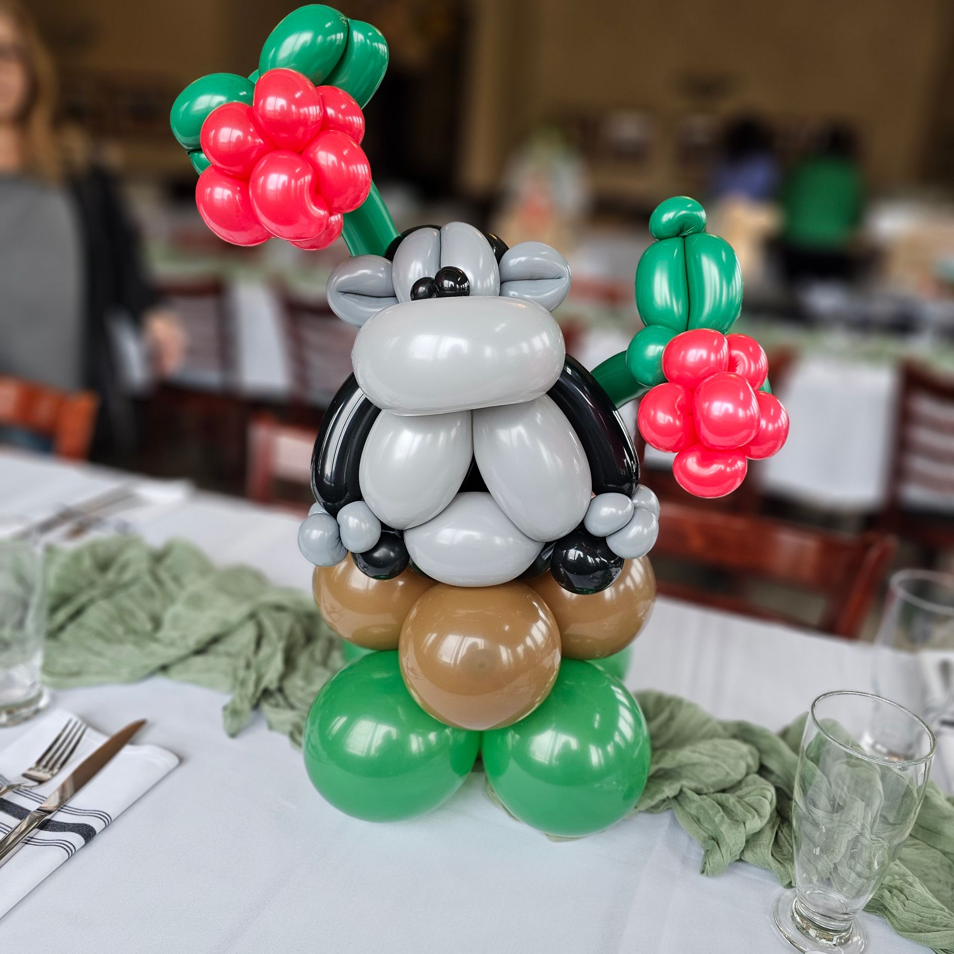 Balloon sculpture of a cow with green and red berries on a table.