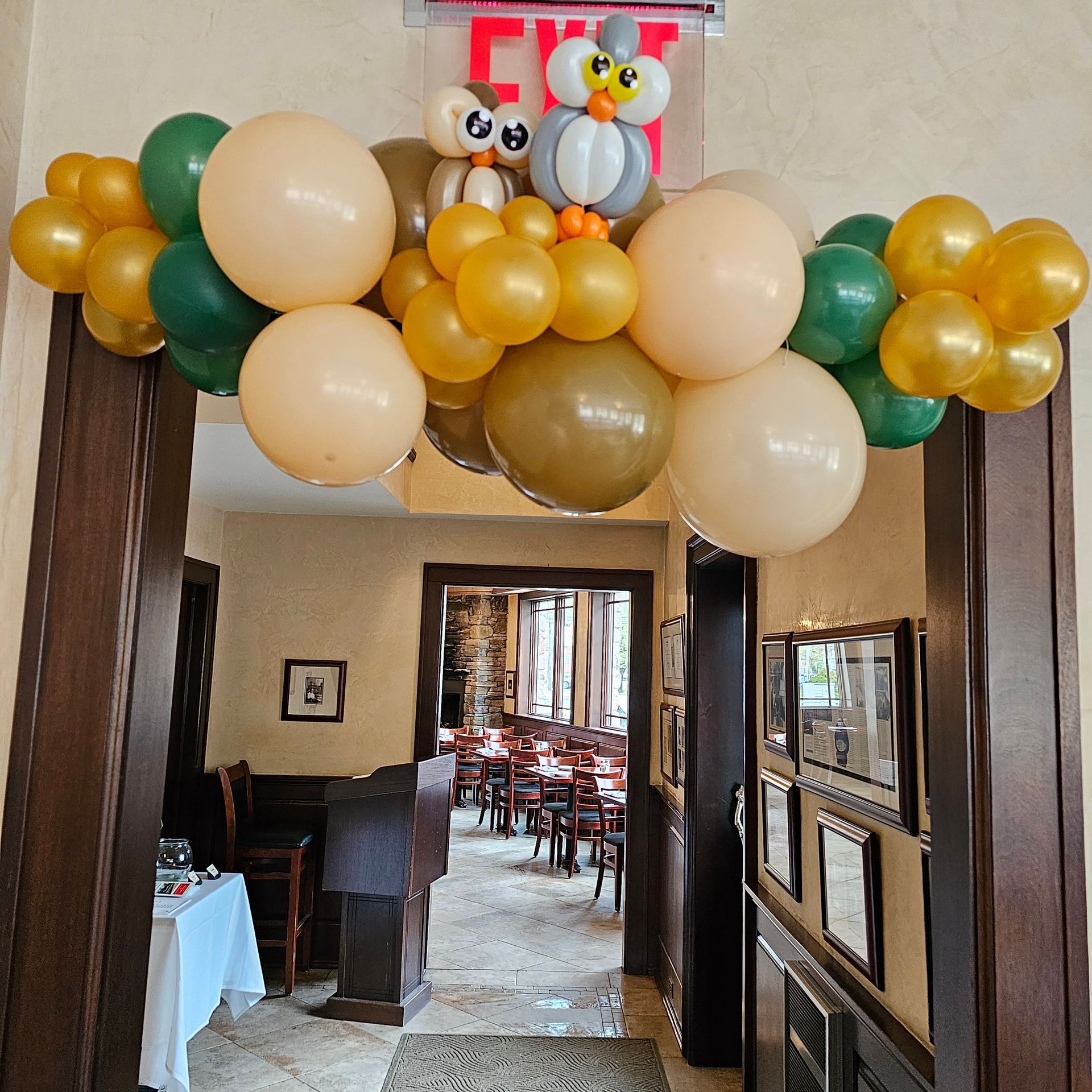 Archway decorated with gold, beige, and green balloons, with owl balloon figures and an Exit sign.