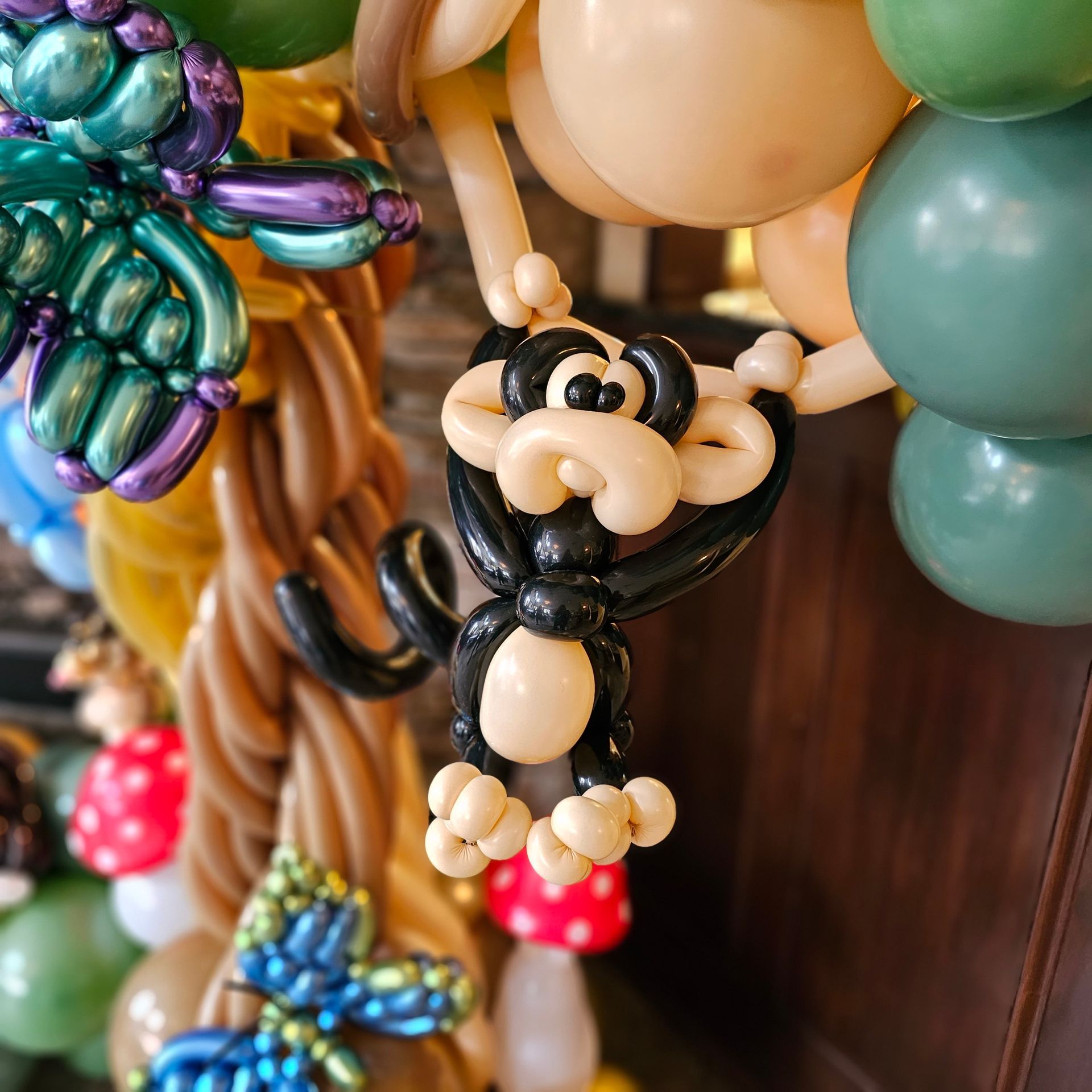 Balloon monkey hanging from a balloon tree, part of an elaborate balloon decoration with other forest elements.