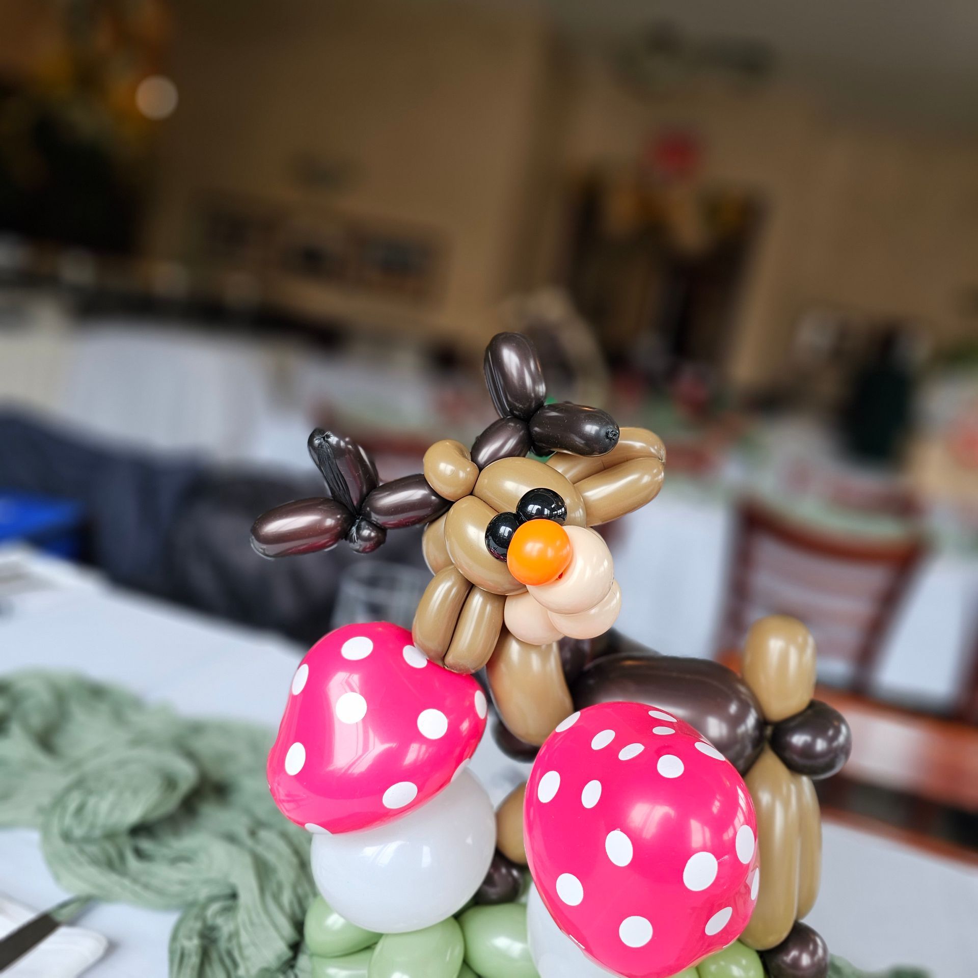 Balloon sculpture of a reindeer with mushroom decorations. Brown and pink balloons, indoors.