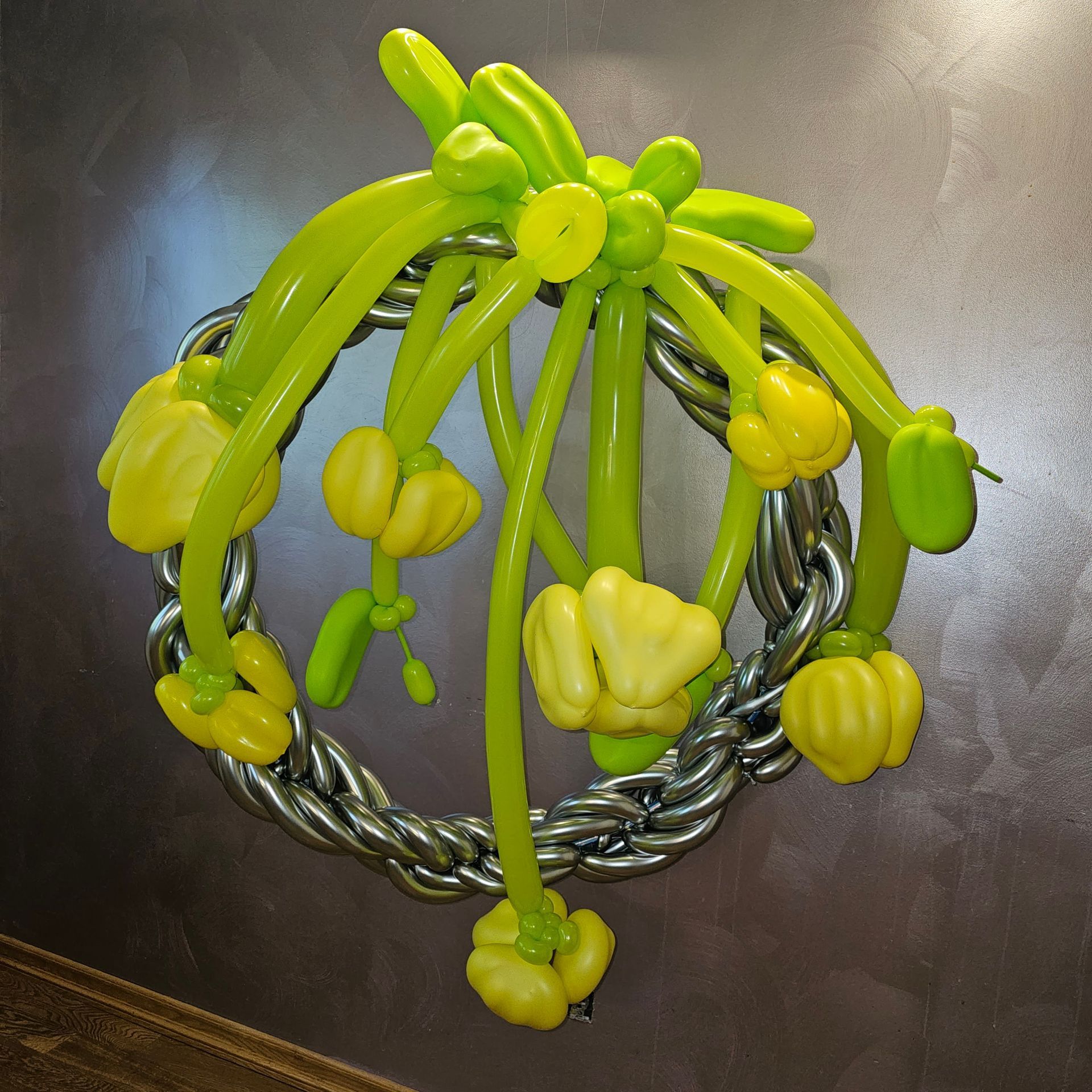 A balloon wreath with yellow and green balloons in front of a gray wall.