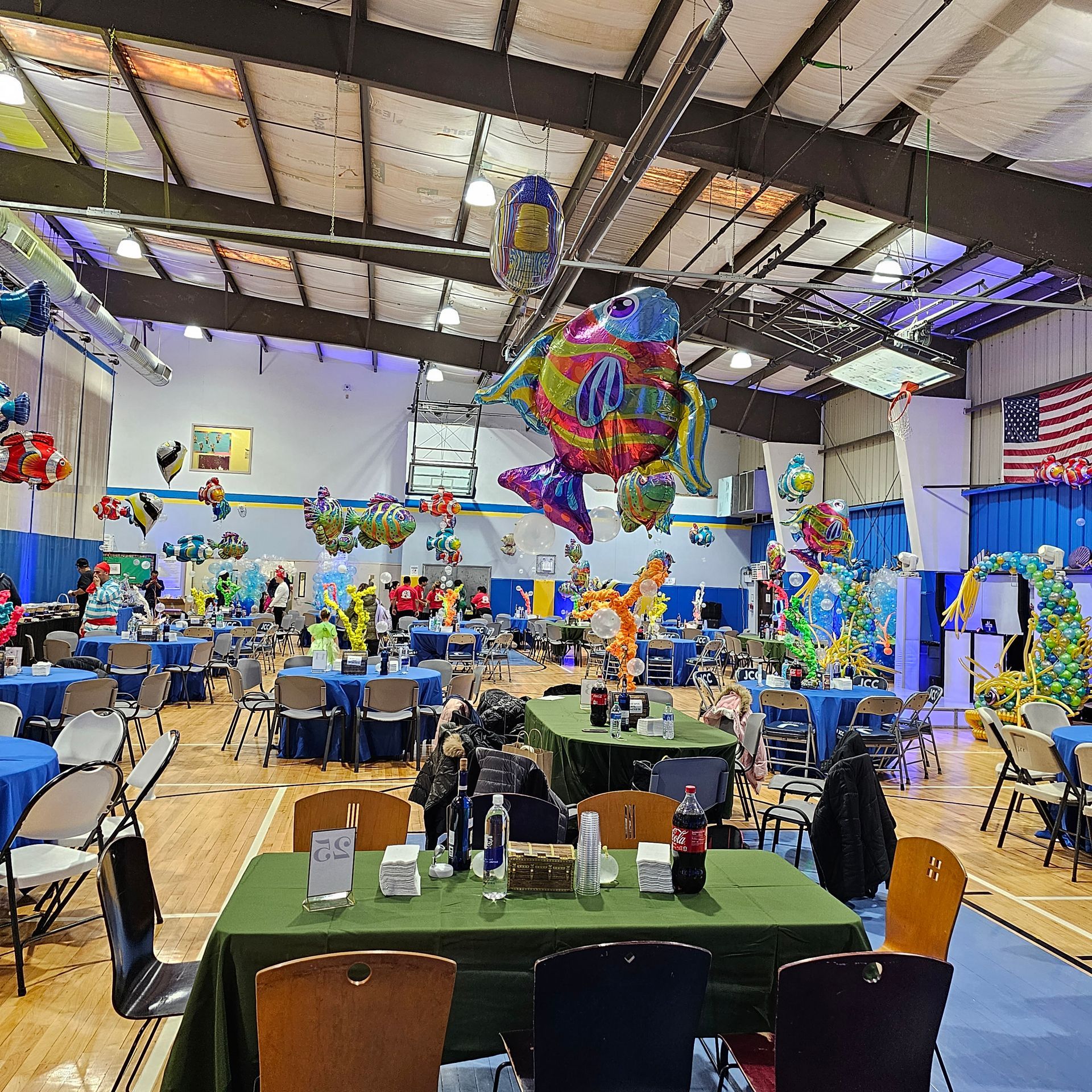 Indoor event hall decorated with balloons and tables, American flag visible.