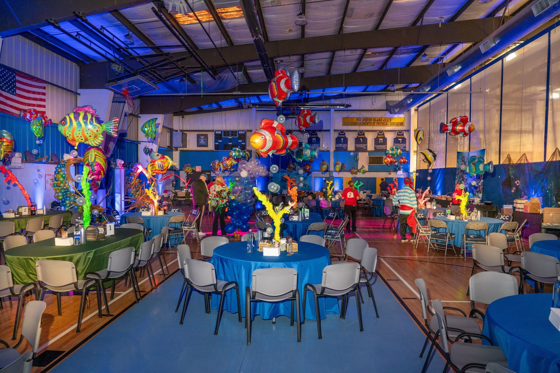 Event hall with tables, chairs, and ocean-themed decorations, including balloons and blue and green colors.