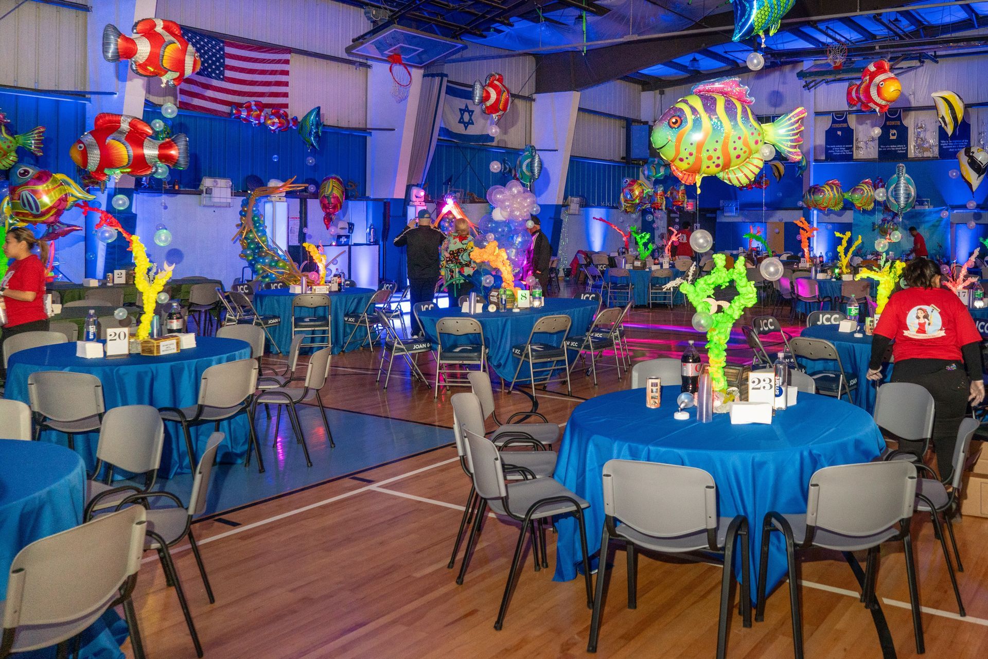Blue-themed party with fish decorations and tables. People are present, set in a gymnasium. American flag visible.