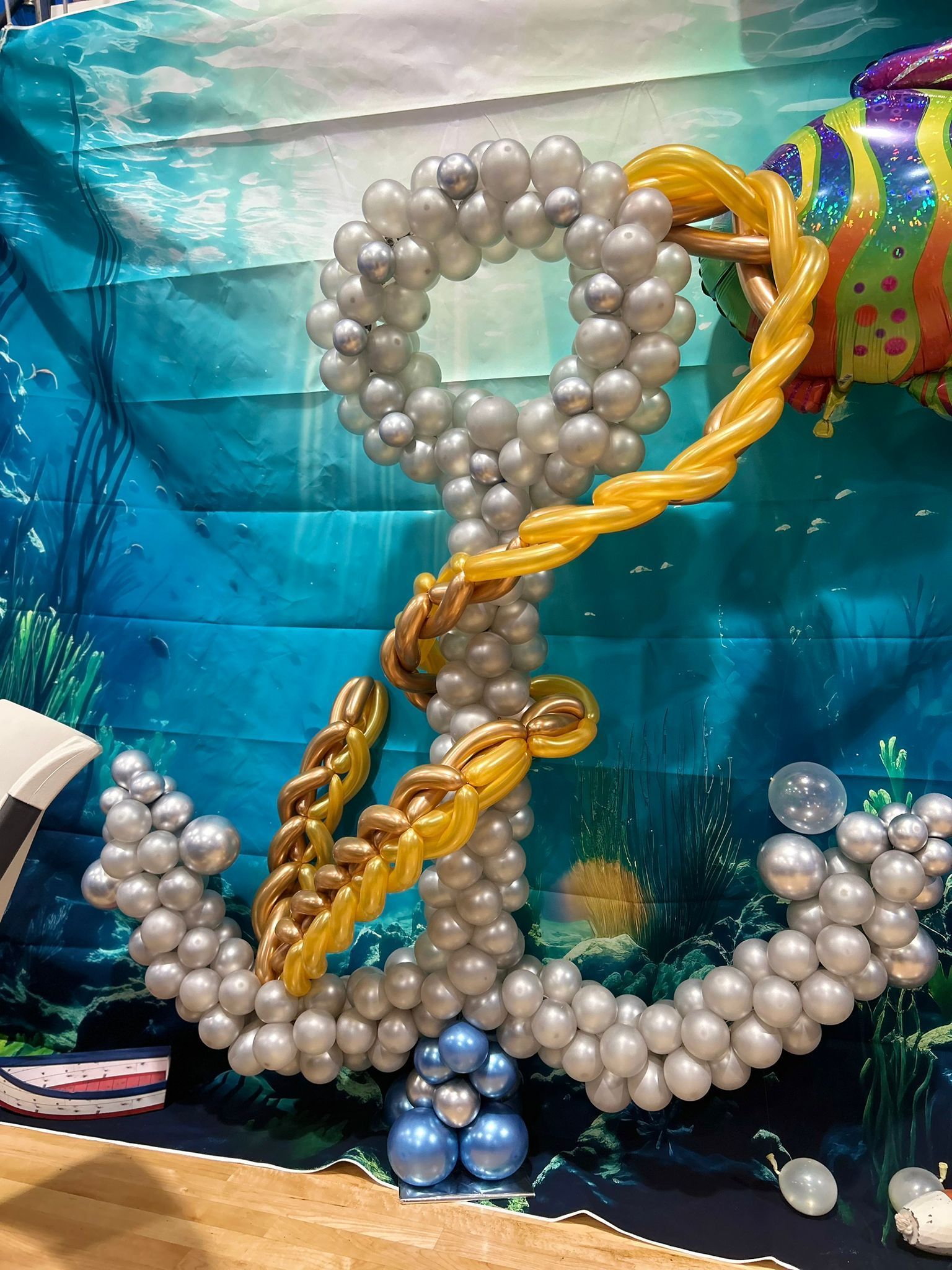 Balloon sculpture of an anchor with silver and gold balloons against an ocean backdrop.