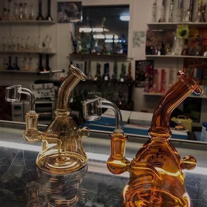 Two amber glass bongs with quartz bangers on a shop counter, shelves of glass art in background.
