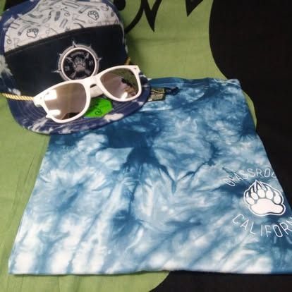 Tie-dye blue t-shirt with a bear paw logo, sunglasses, and a navy and white cap.