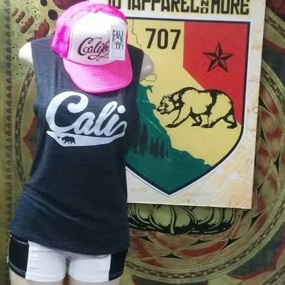 Mannequin wearing a Cali tank top, shorts, and a pink hat, standing in front of a California-themed sign.