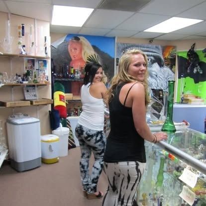 Two women inside a smoke shop looking at merchandise. One smiles, the other looks back. Colorful art on the walls.