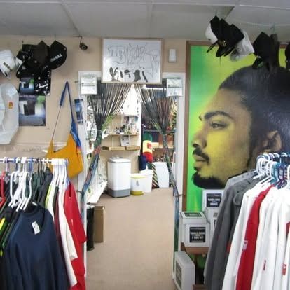 Interior of a retail store with clothing racks and fishing rods. A large portrait of a man on right.