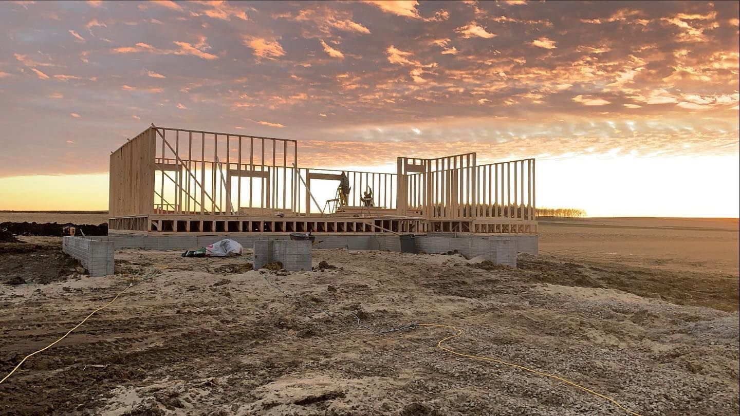 Framing of a new house on a concrete foundation at sunset. Golden sky above a flat, brown field.