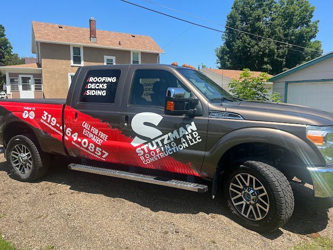 Brown and red Stutzman Construction truck parked in front of a house. The truck has roofing, deck, and siding advertisements.
