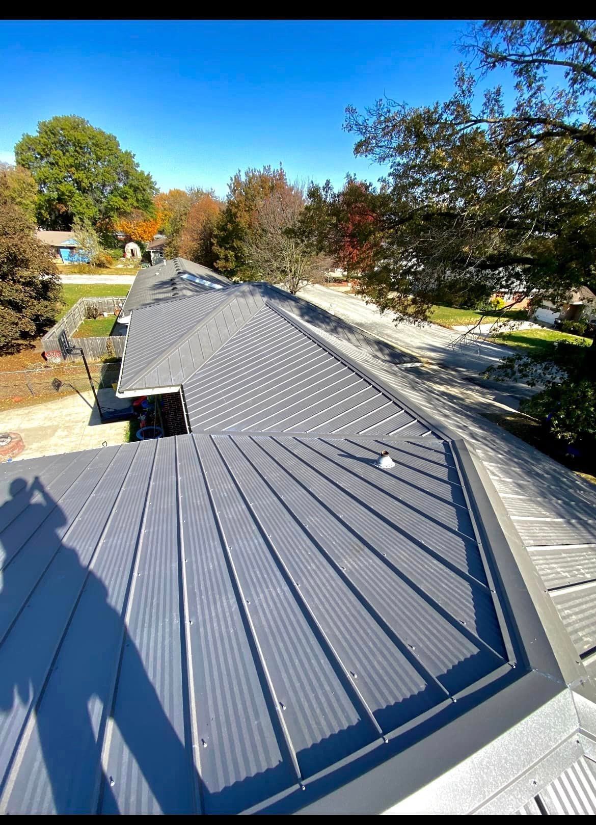 View of a newly installed gray metal roof on a house, with autumn trees and blue sky in the background.
