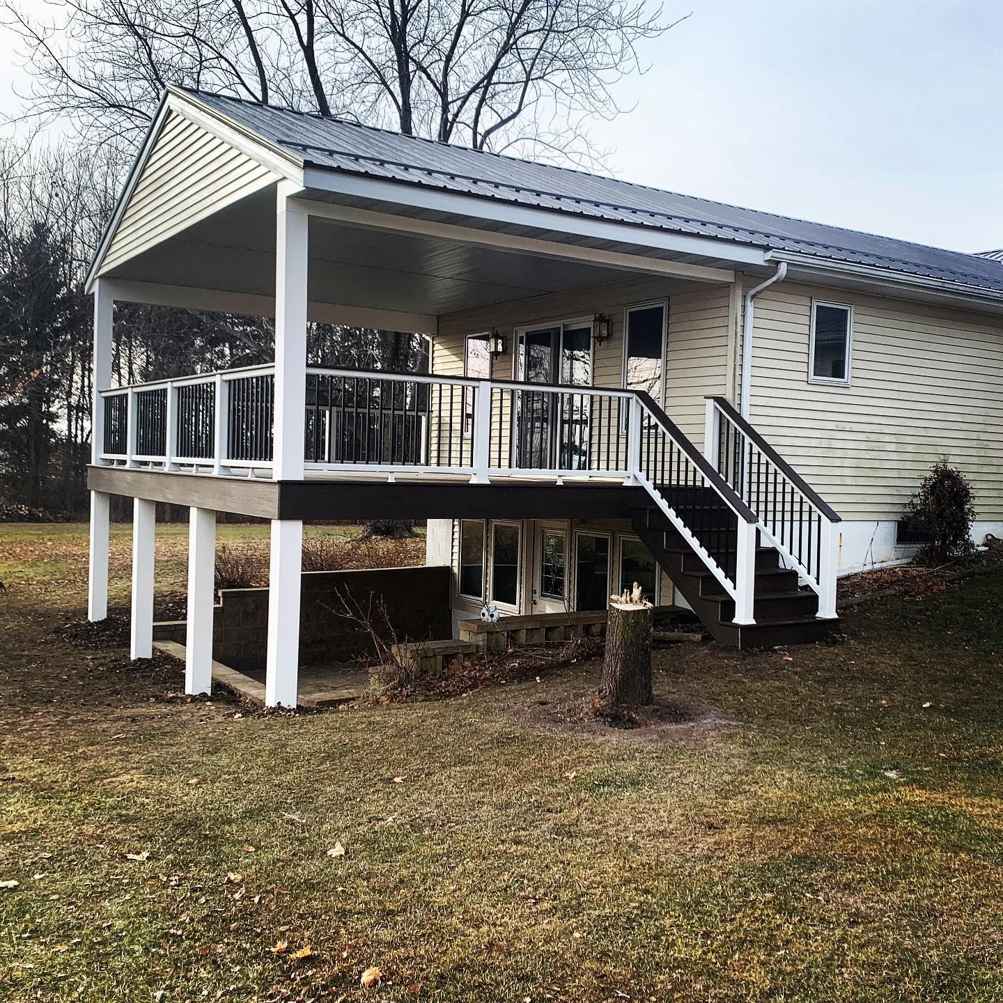 Raised deck attached to a light-colored house with a metal roof. The deck has stairs and a covered portion supported by white columns.