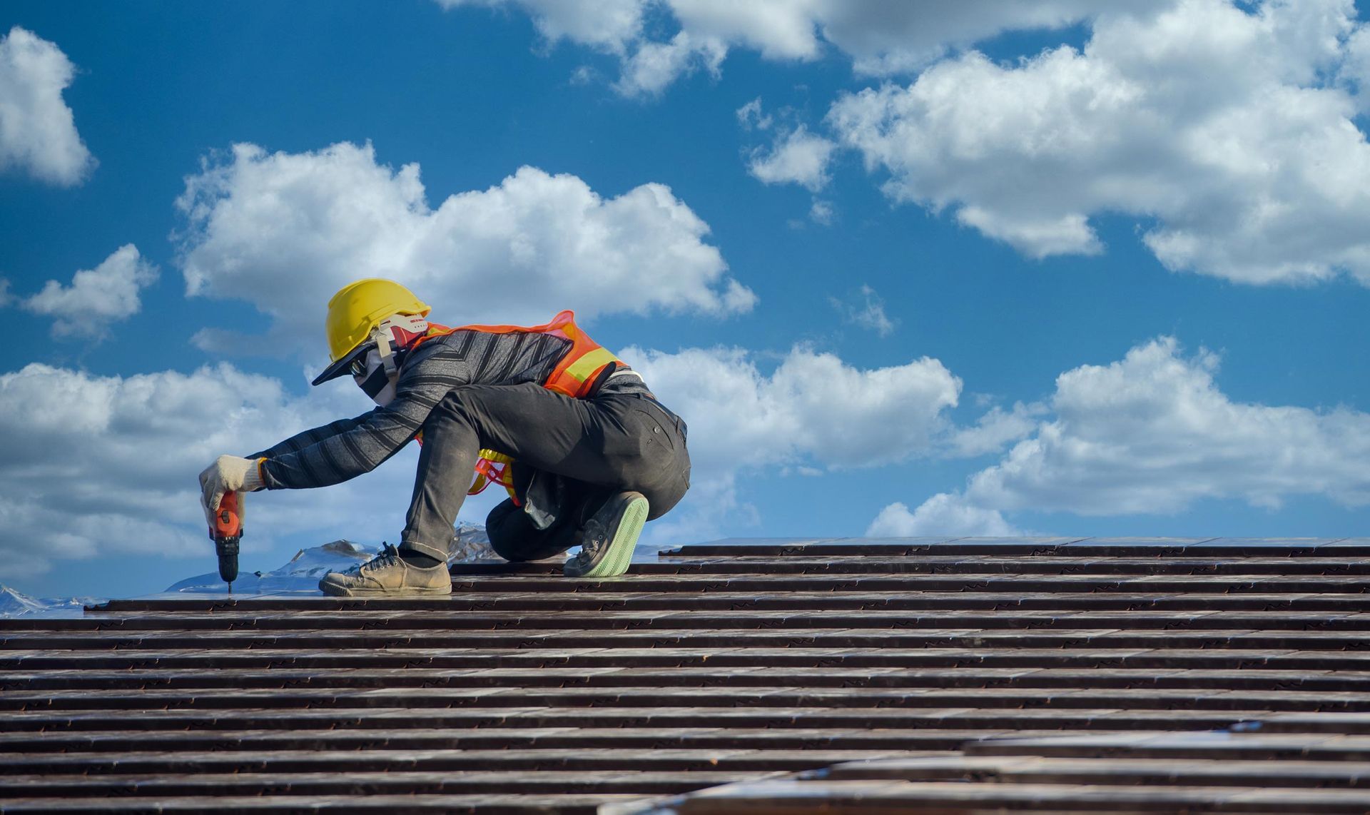 A roofing installation contractor is working on a roof with a bright blue sky above.