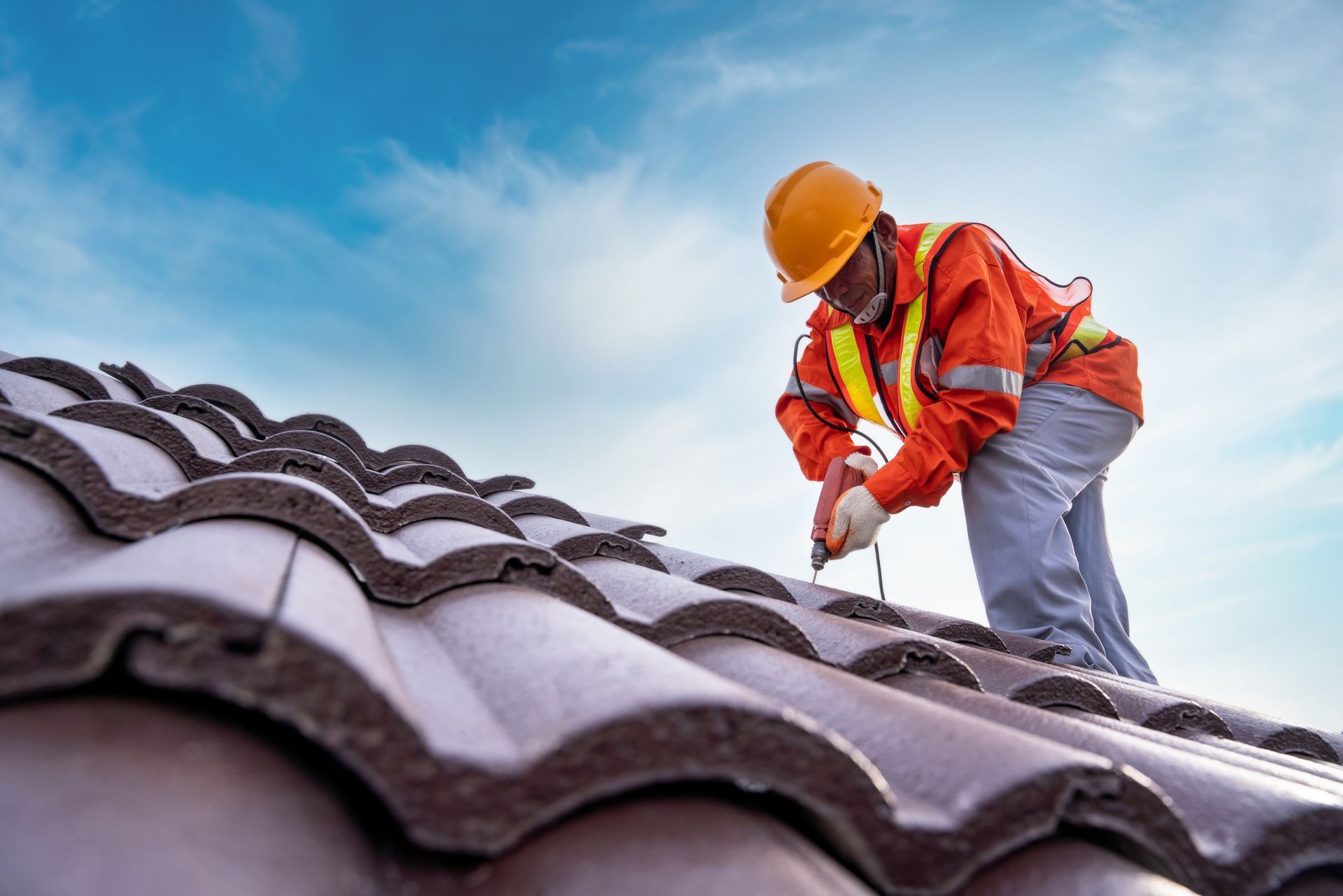 A residential roofing contractor, equipped with safety gear, is working on installing a roof.