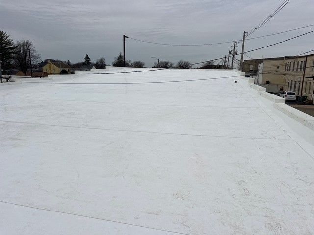 A flat, white roof covers a building, with a cloudy sky overhead. Power lines run across the top.