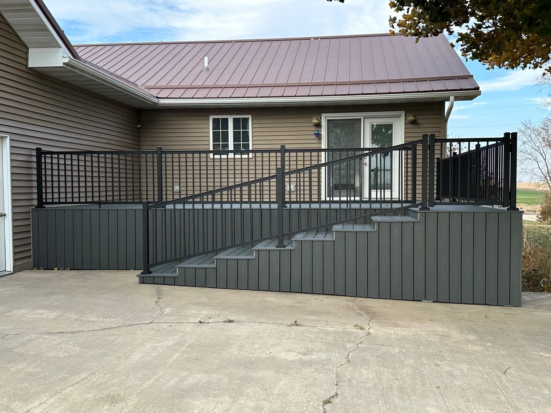 Gray deck with black railing and steps attached to a brown house with a metal roof.