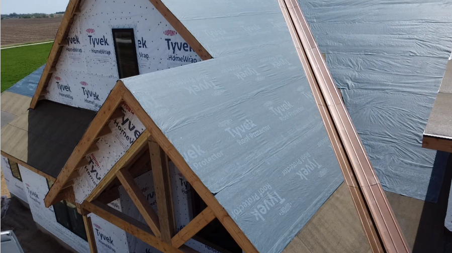 A house under construction with a wood frame, covered in Tyvek wrap on the roof and walls.