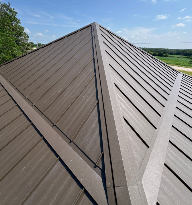 Brown metal roof with ridges and angled edges under a clear blue sky.