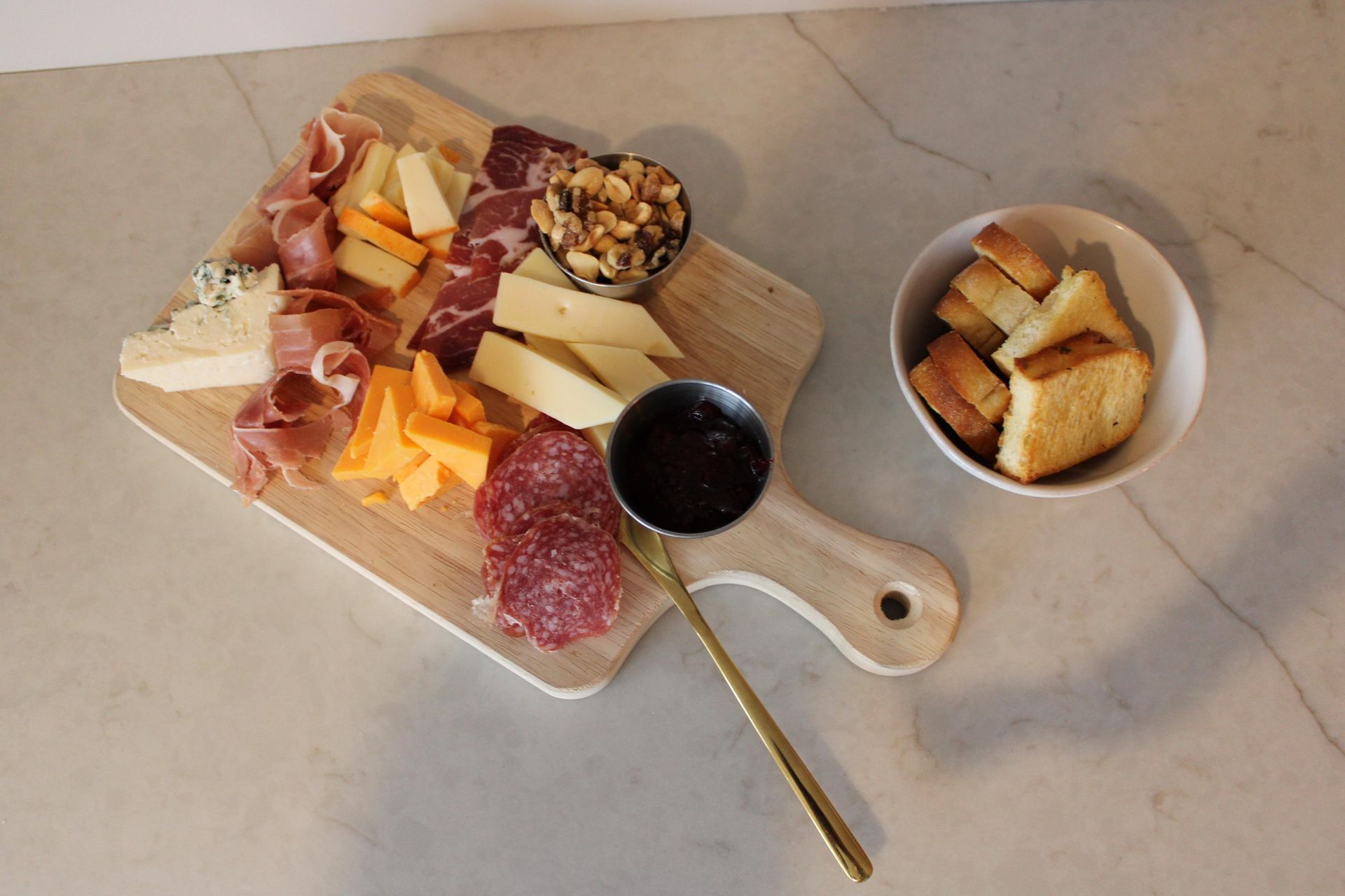 A wooden cutting board filled with meat and cheese next to a bowl of bread.