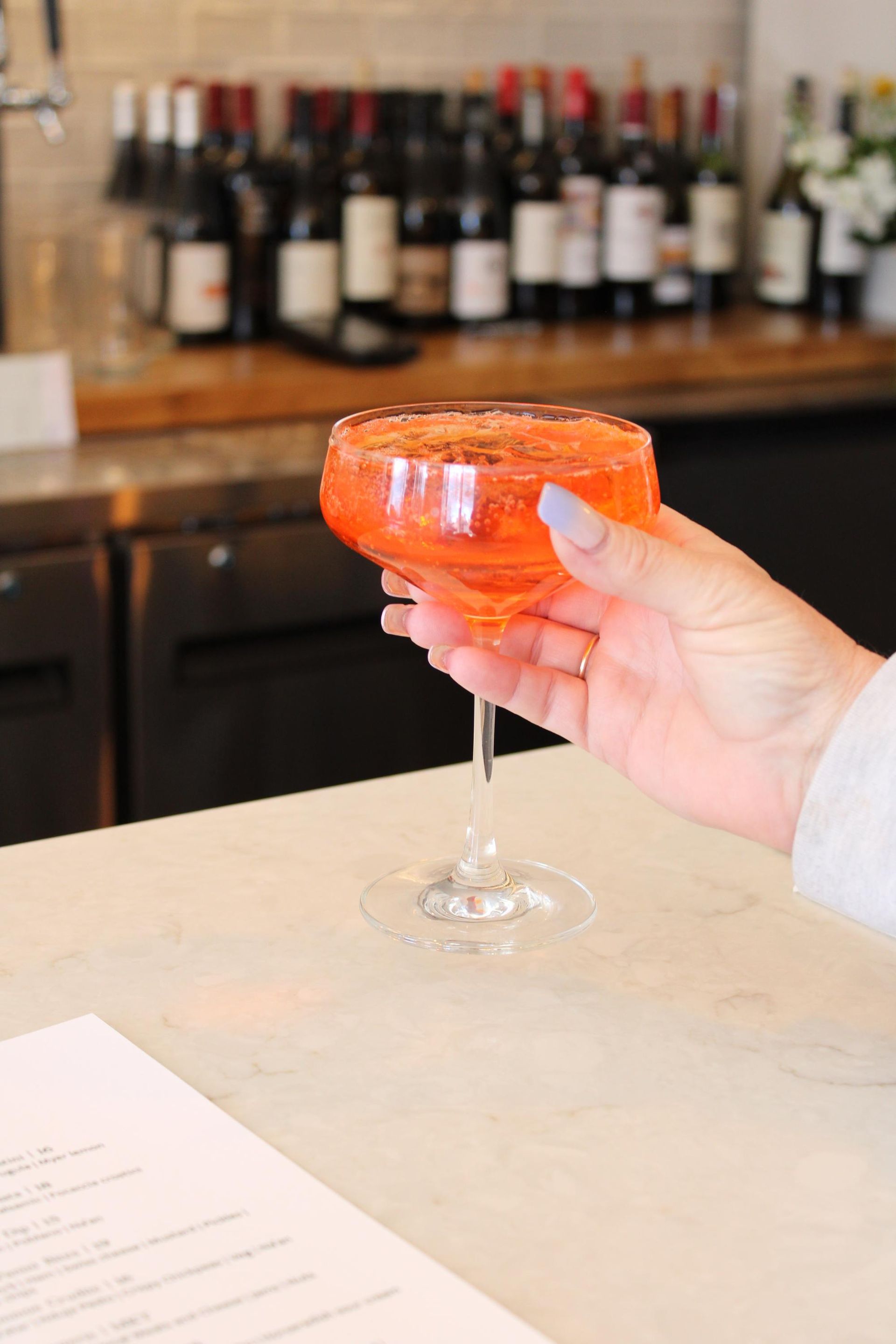 A person is holding a glass of orange liquid on a counter.