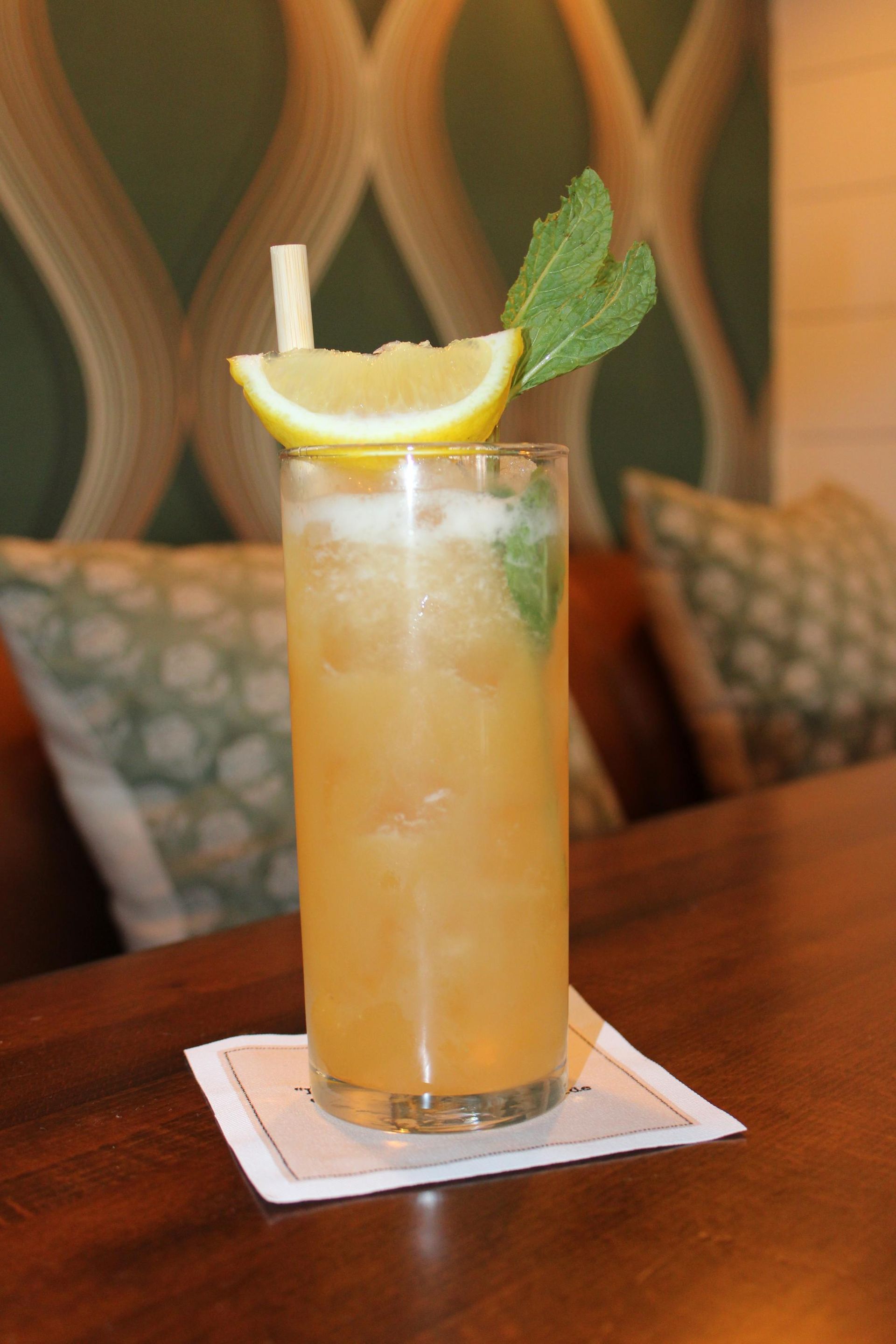 A drink in a tall glass with a straw and a slice of lemon
