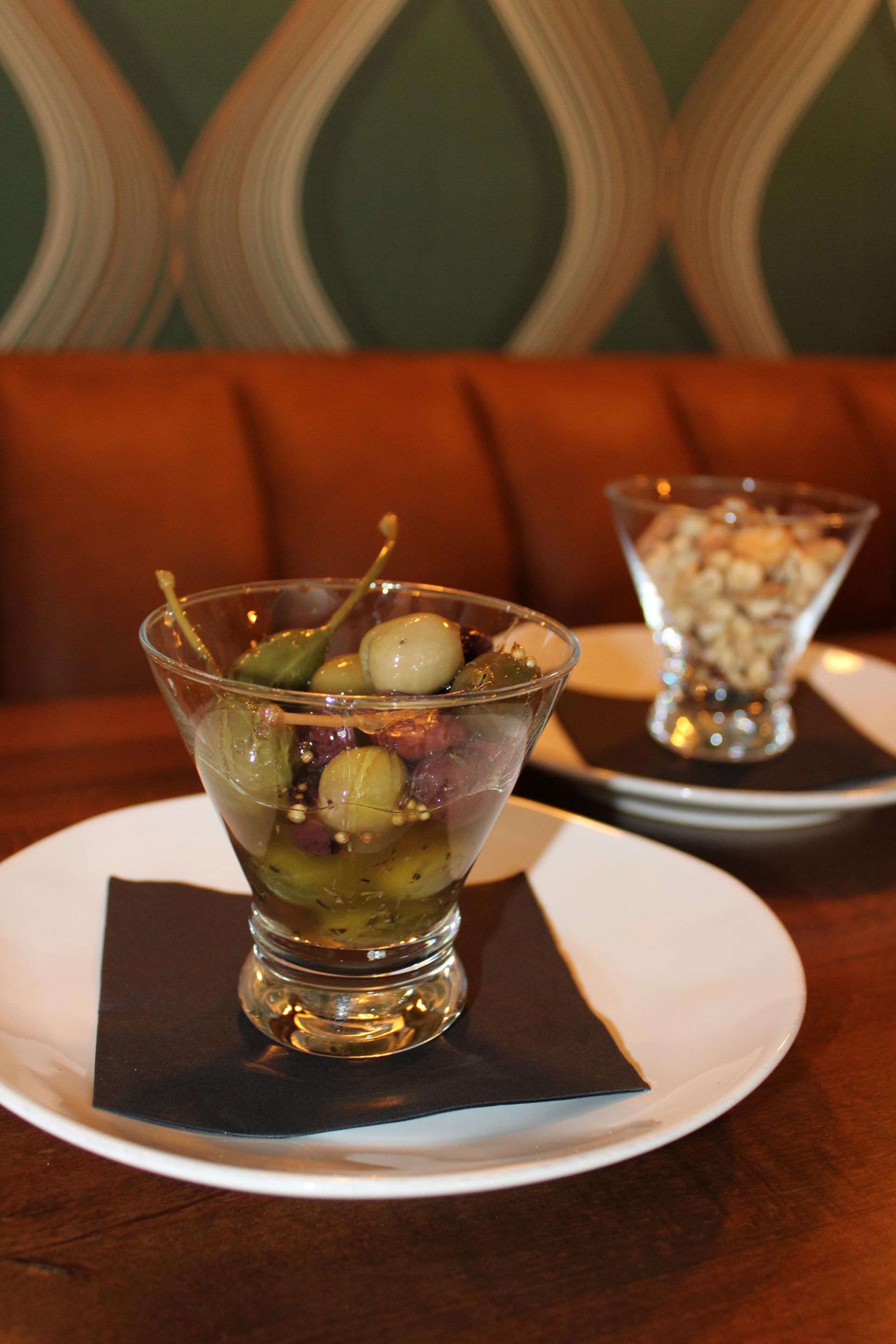 A martini glass filled with olives next to a bowl of nuts