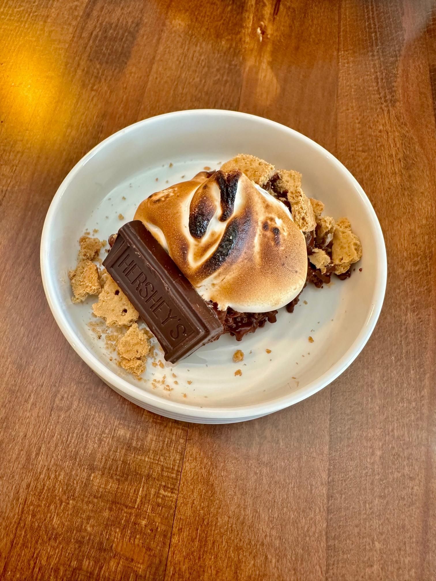A plate of s'mores with a chocolate bar on a wooden table.