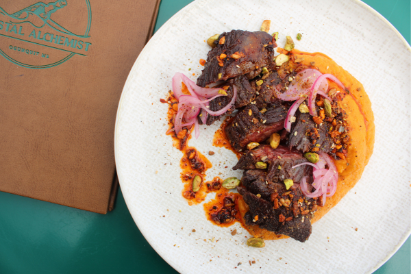 A wooden cutting board topped with a variety of food including pickles , olives and bread.