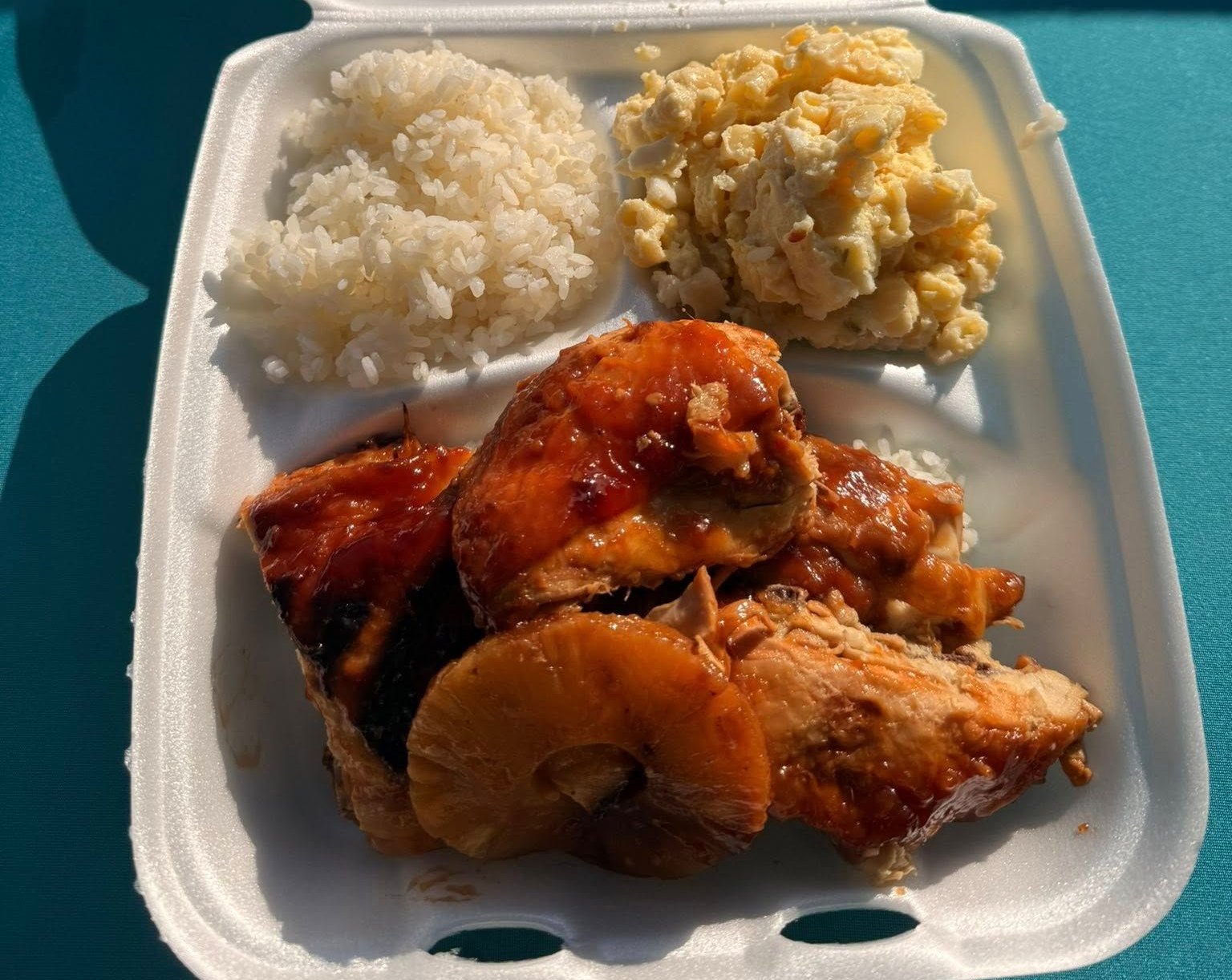 Chicken with pineapple slices, rice, and macaroni salad in a styrofoam container.