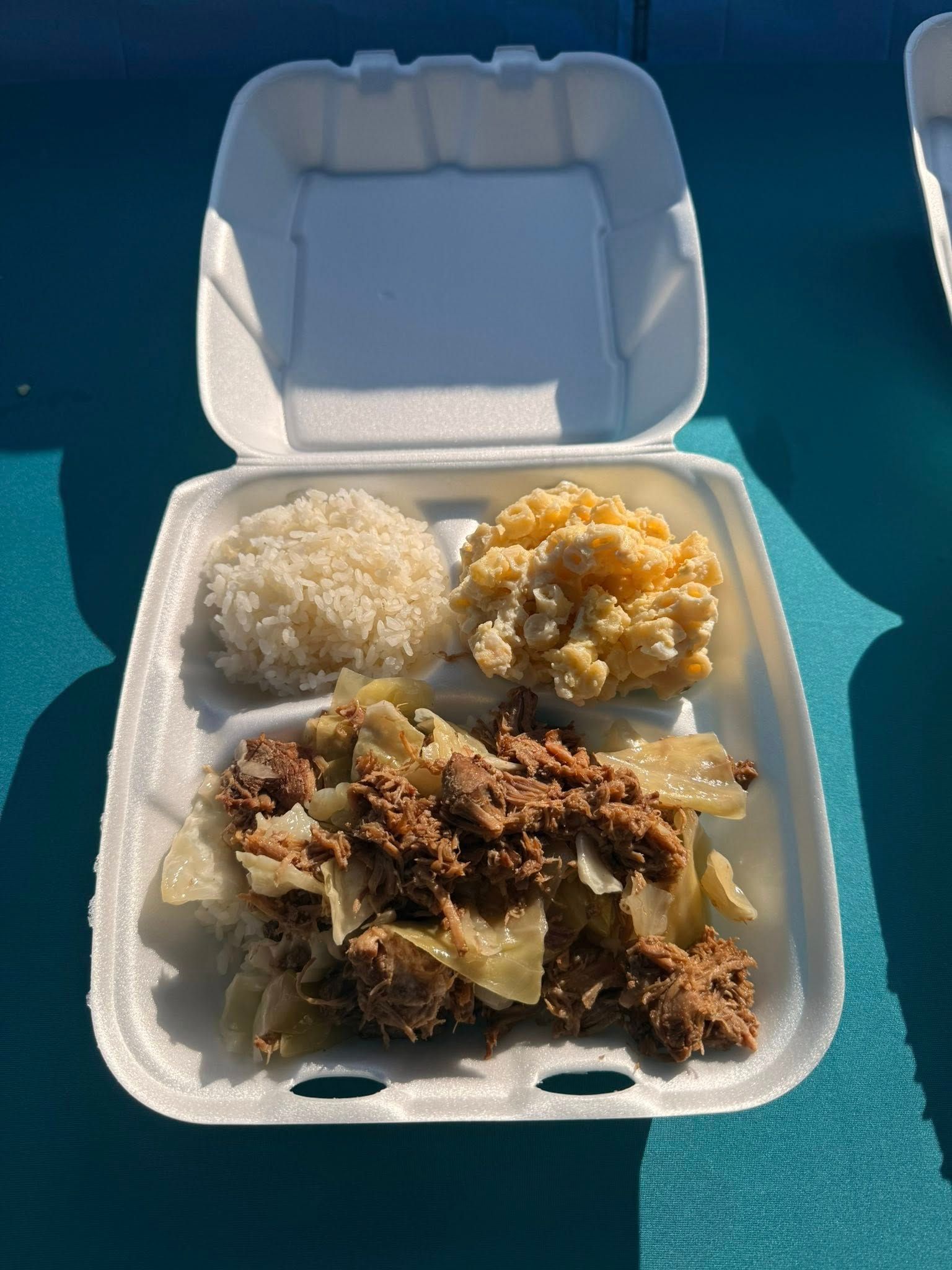 Plate of food: rice, macaroni salad, and shredded meat with cabbage in a foam container.