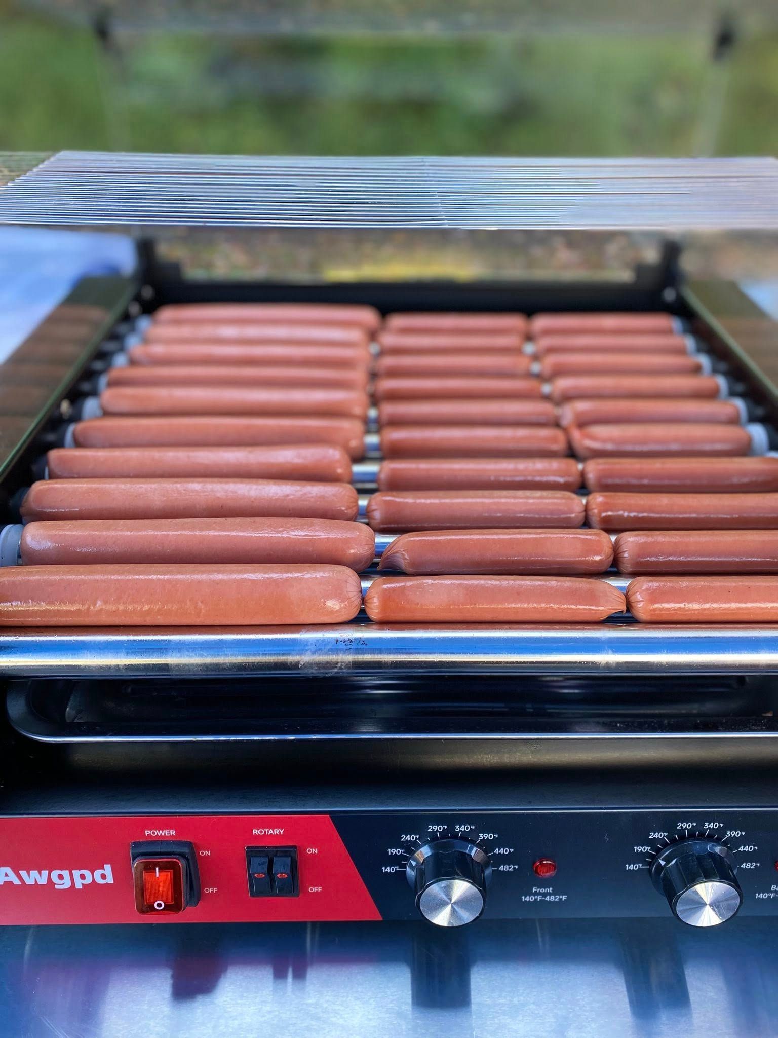 Hot dogs cooking on a roller grill with red base and controls.