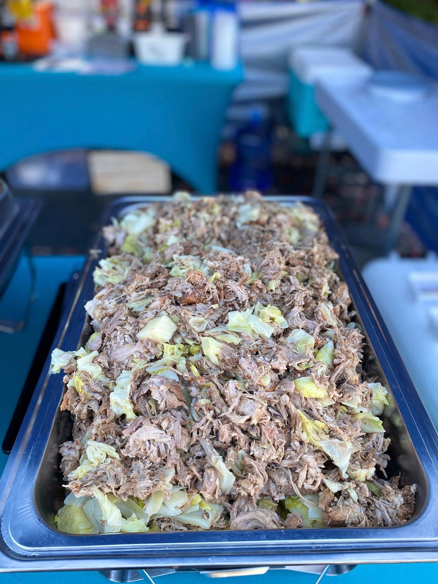 Tray of shredded meat with cabbage; outdoors, blue table, party food.