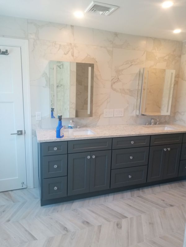 Gray bathroom vanity with marble countertop, two mirrors, and patterned floor.