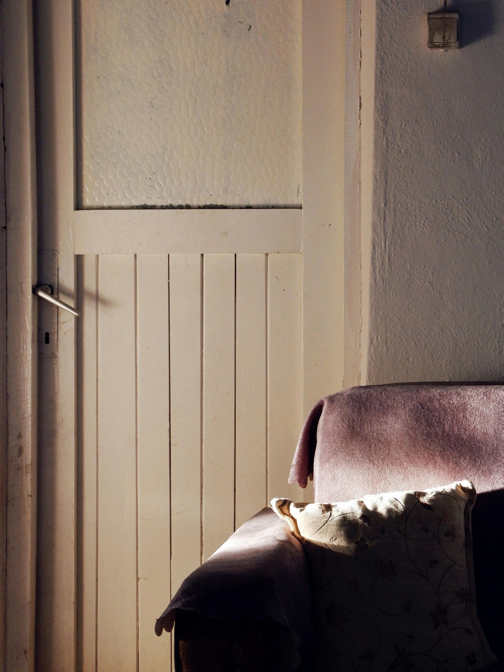White-painted wooden door slightly ajar, casting a shadow. A blanket and pillow rest on a chair nearby.
