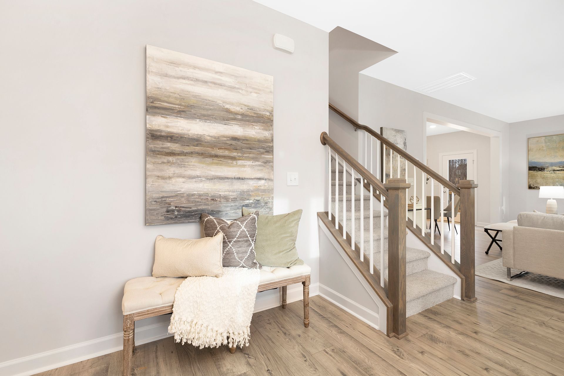 A living room with hardwood floors , a bench , stairs and a painting on the wall.