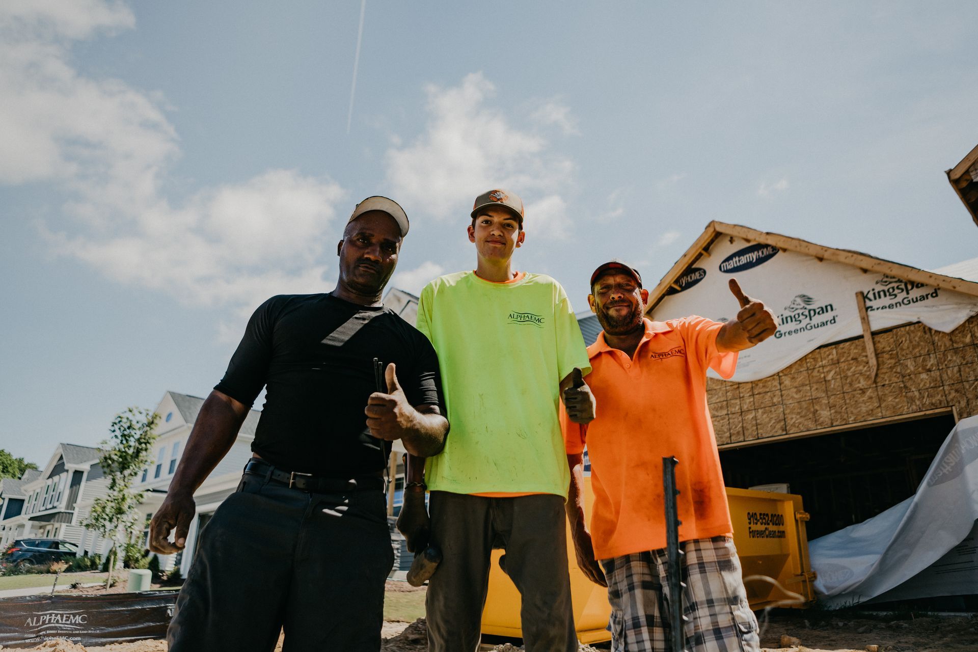 Three men smiling and holding cards. Landscapers in front of a house.