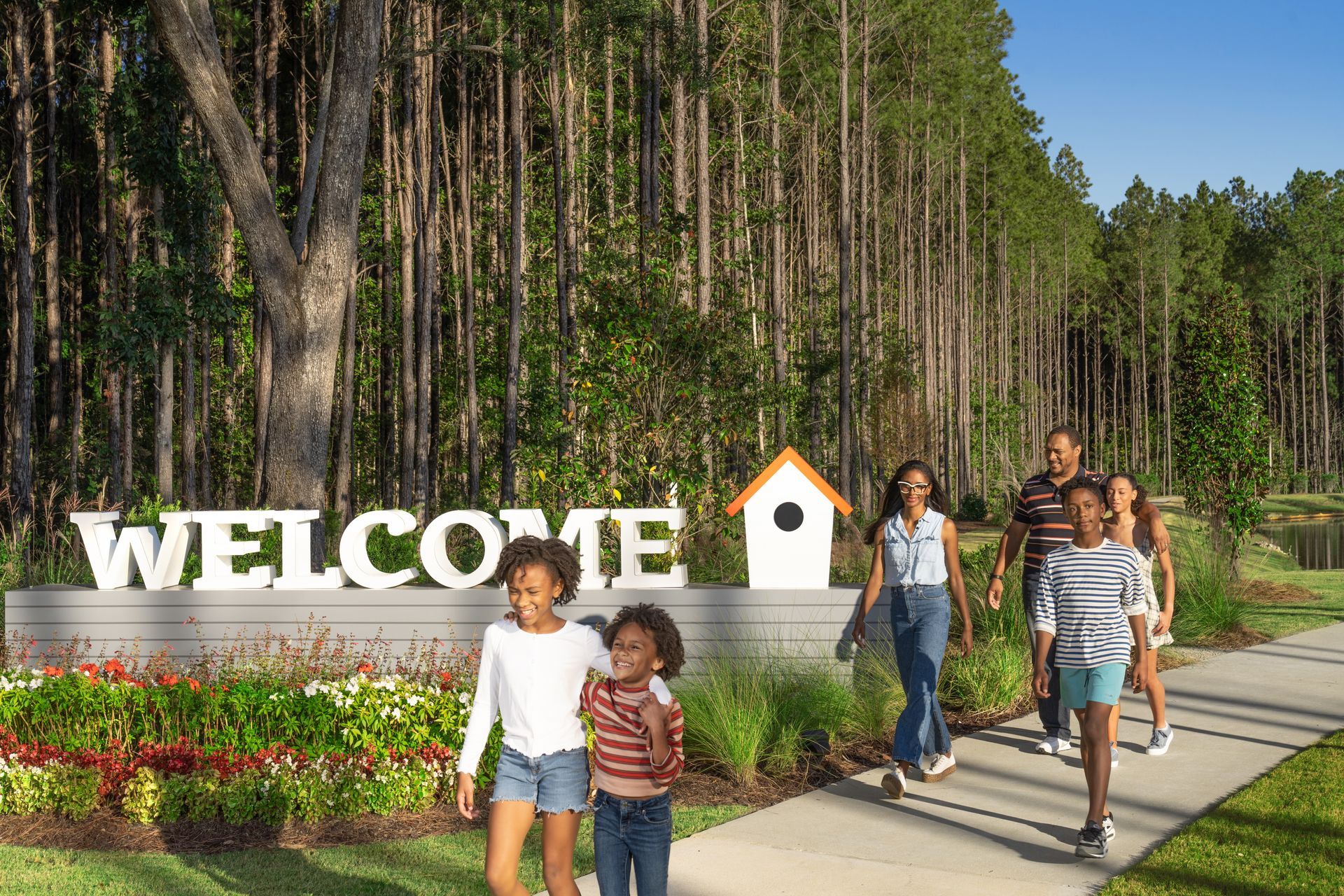 A family is walking down a sidewalk in front of a welcome sign.