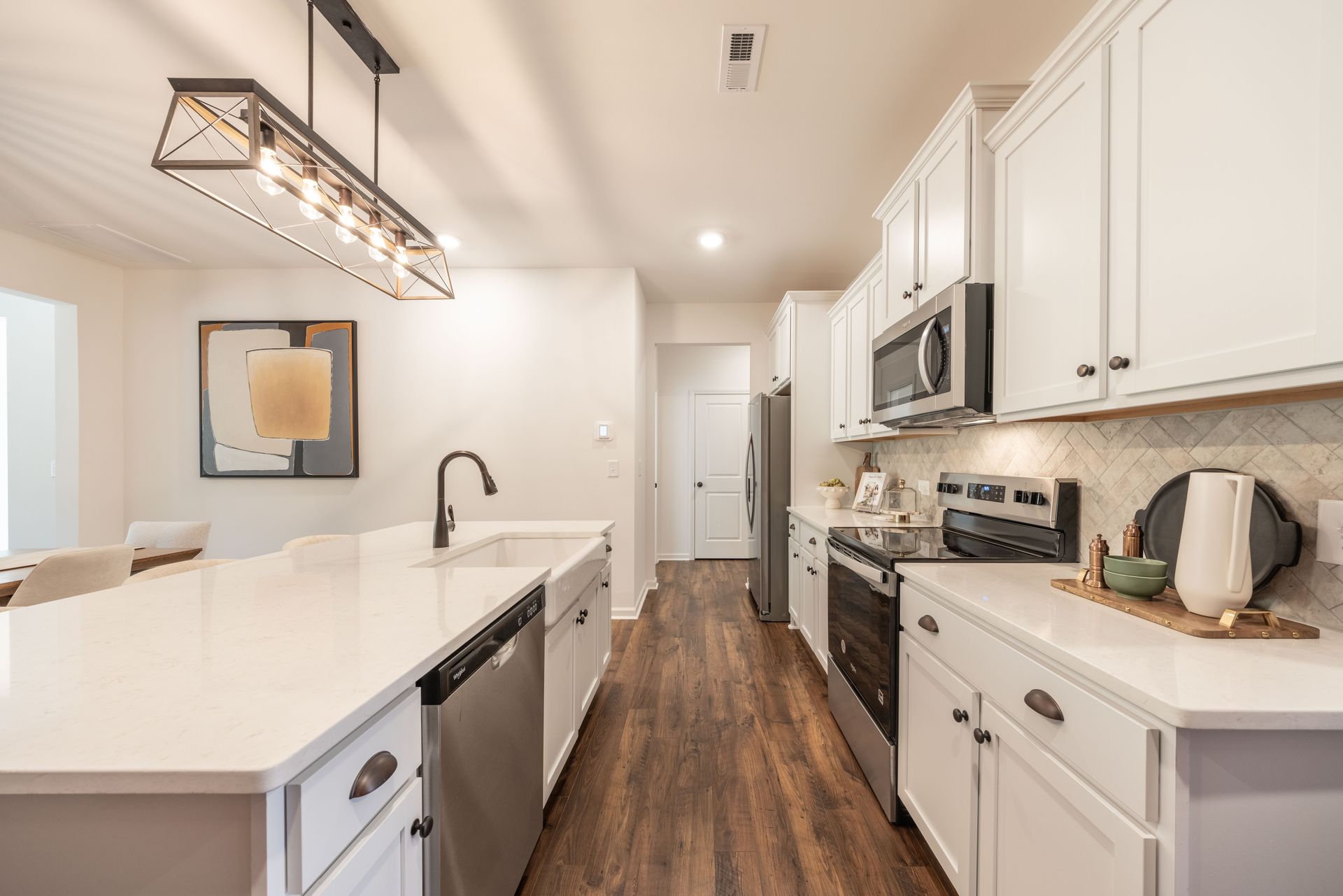 A kitchen with white cabinets , stainless steel appliances , and hardwood floors - Abigale Floorplan by True Homes.